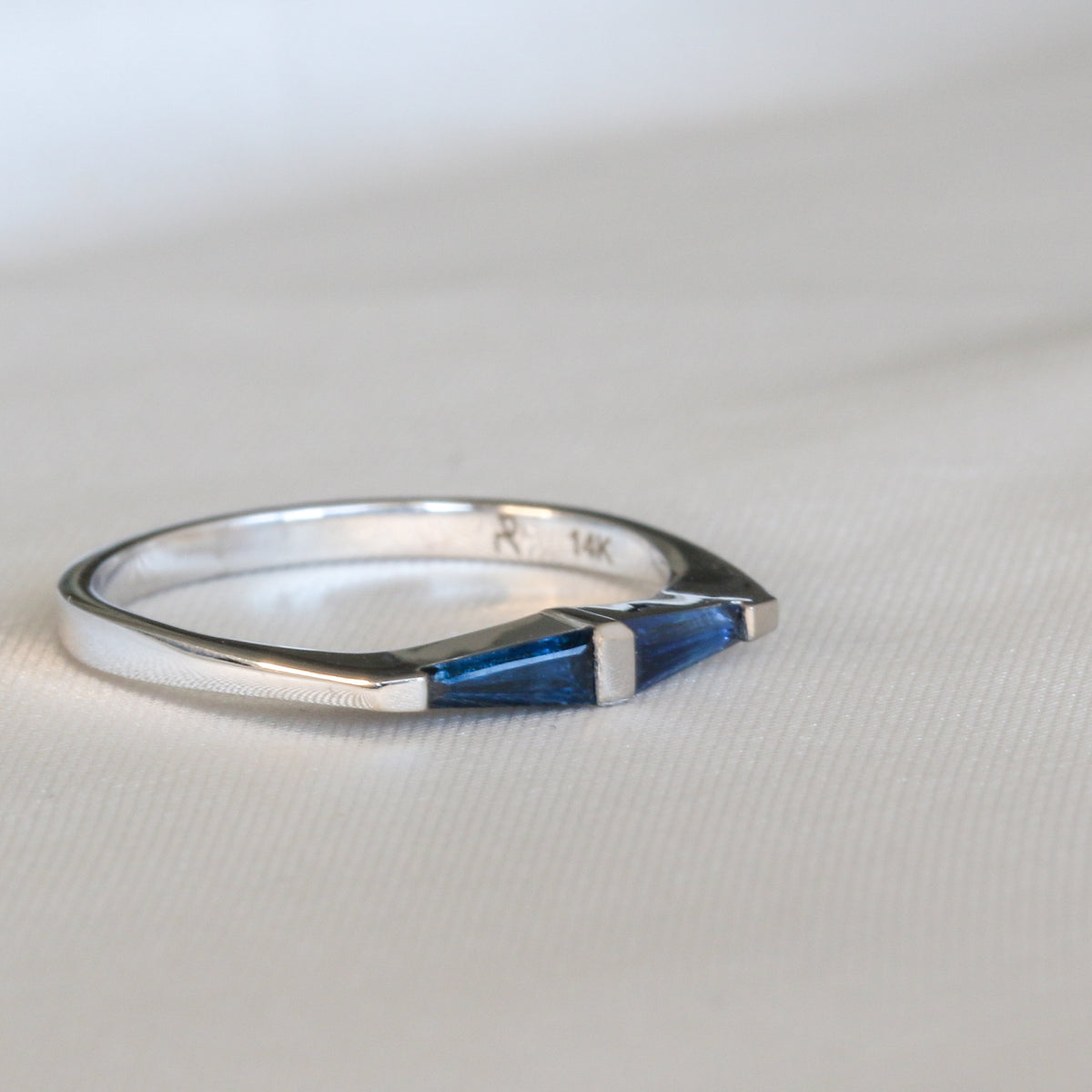 14K white gold ring with two tapered baguette blue sapphires mirrored around a gold bar, on white