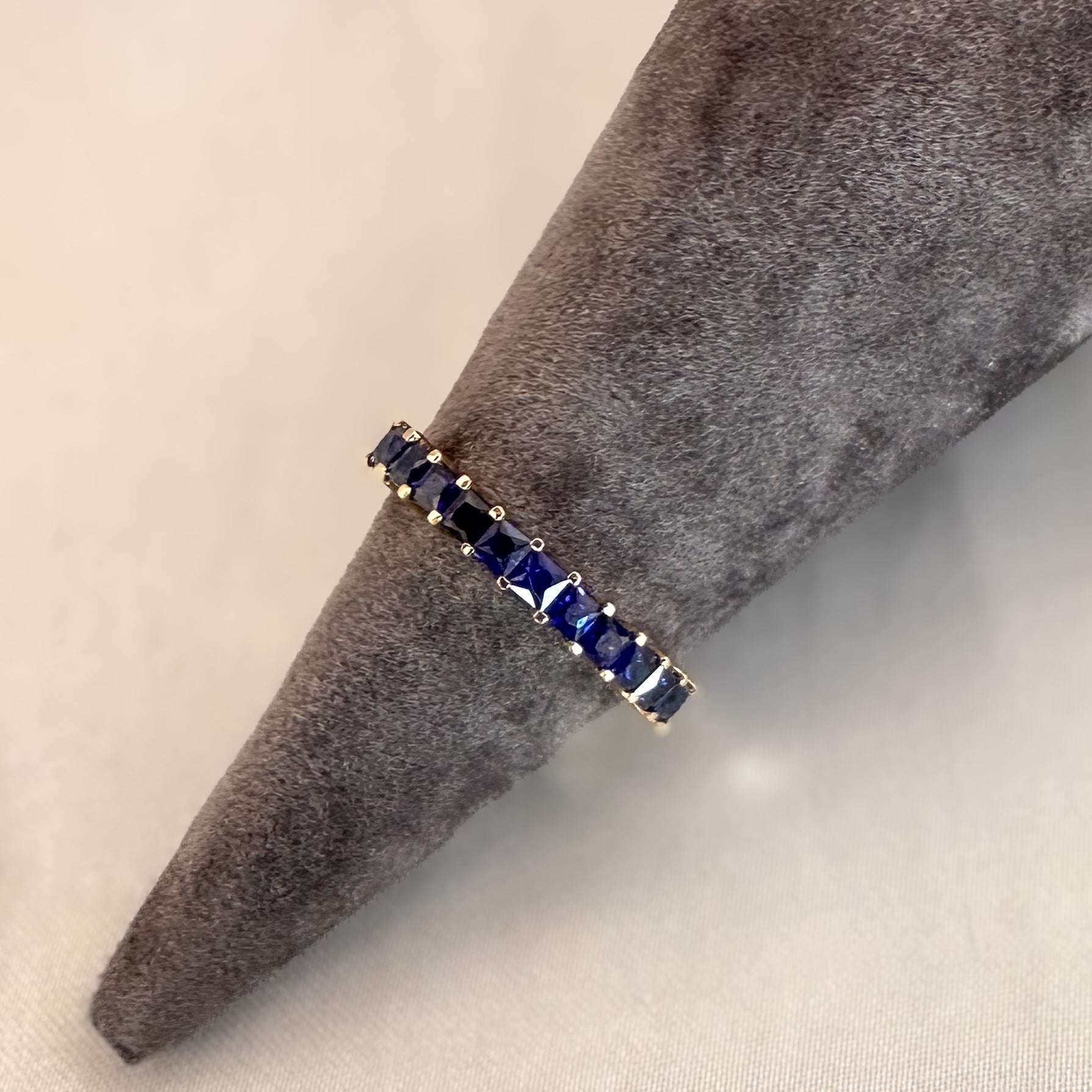  princess cut blue sapphire eternity ring displayed in gray ring stand on white background
