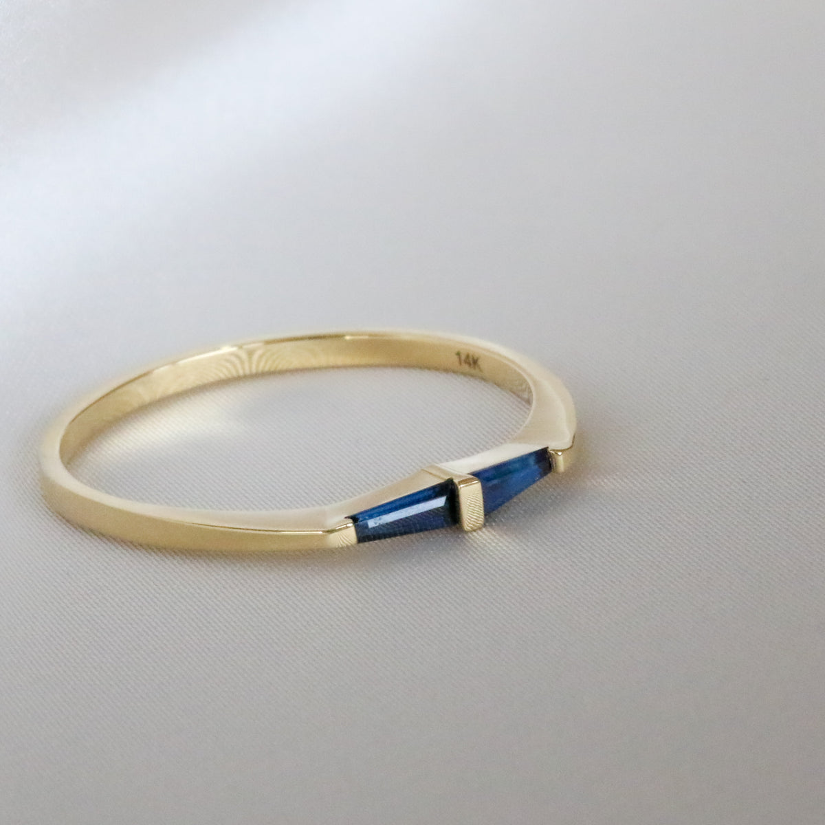 14K yellow gold ring with two tapered baguette blue sapphires mirrored around a gold bar, on white