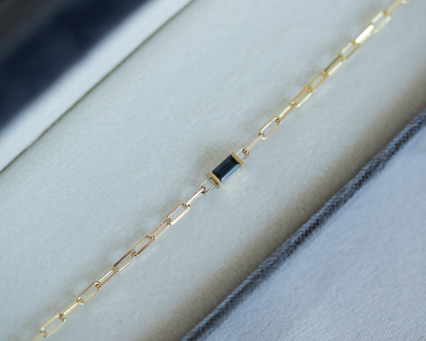 Gold bracelet with a blue baguette cut sapphire on white background