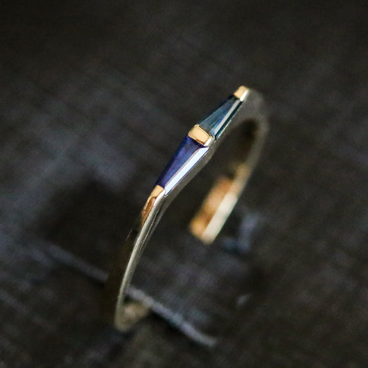 14K yellow gold ring with two tapered baguette blue sapphires and a gold bar between them, on dark fabric