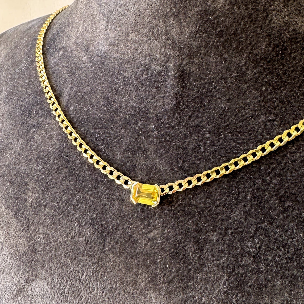 Emerald cut yellow sapphire set east-west in a half bezel on a gold curb chain choker, angled view