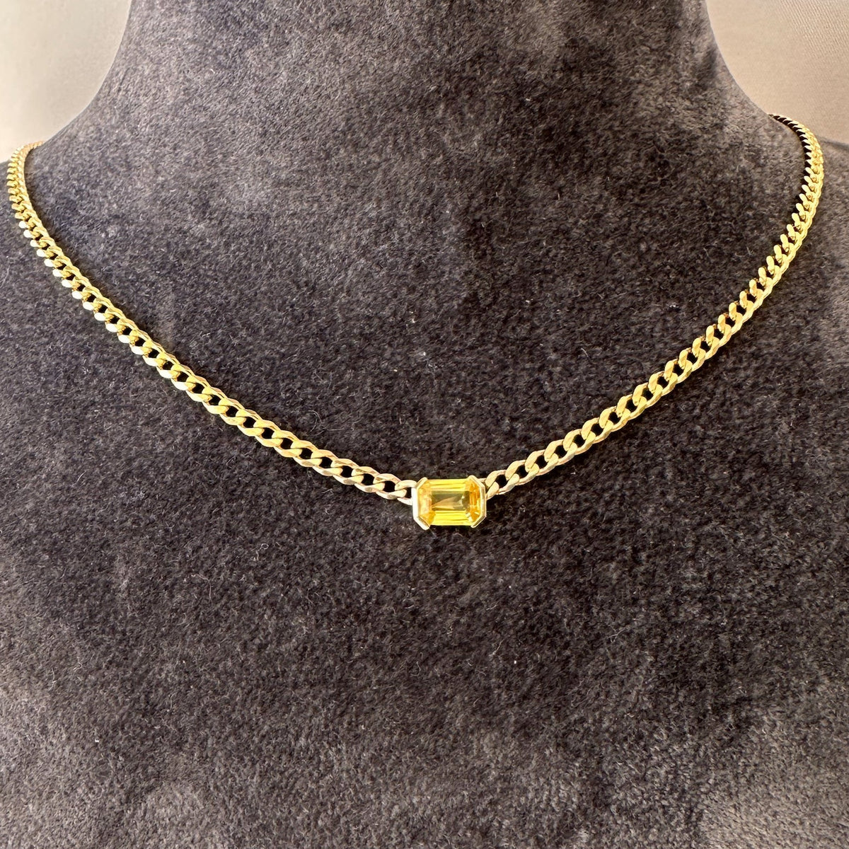 Fine 14K gold curb chain choker with an emerald cut yellow sapphire on a gray jewelry bust